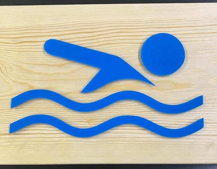 Letrero combinando madera y acrílico azul para señalizar zona autorizada de baño